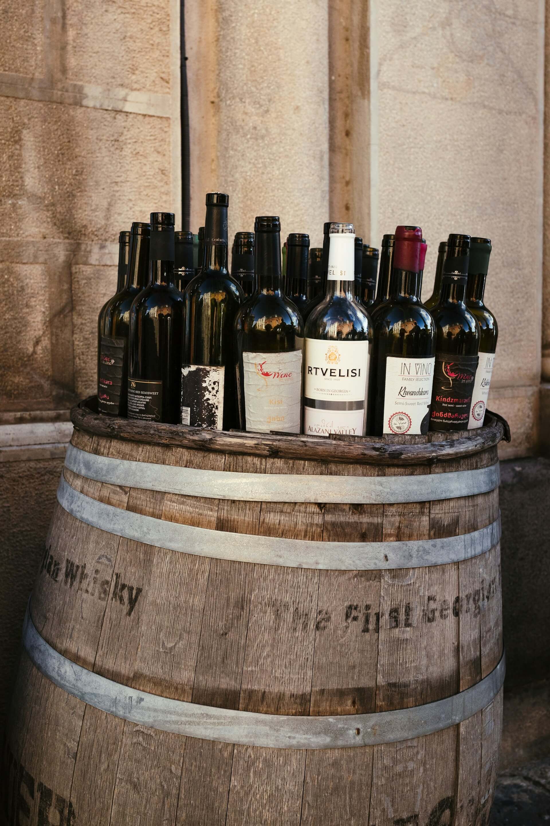 A row of Georgian wine bottles arranged atop an old wooden barrel