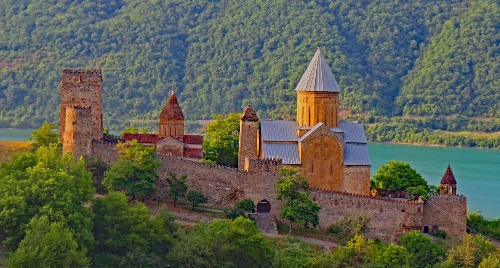 Ananuri fortress - its churches, watchtower and crenellated wall above the turquoise Zhinvali reservoir, wooded hills behind