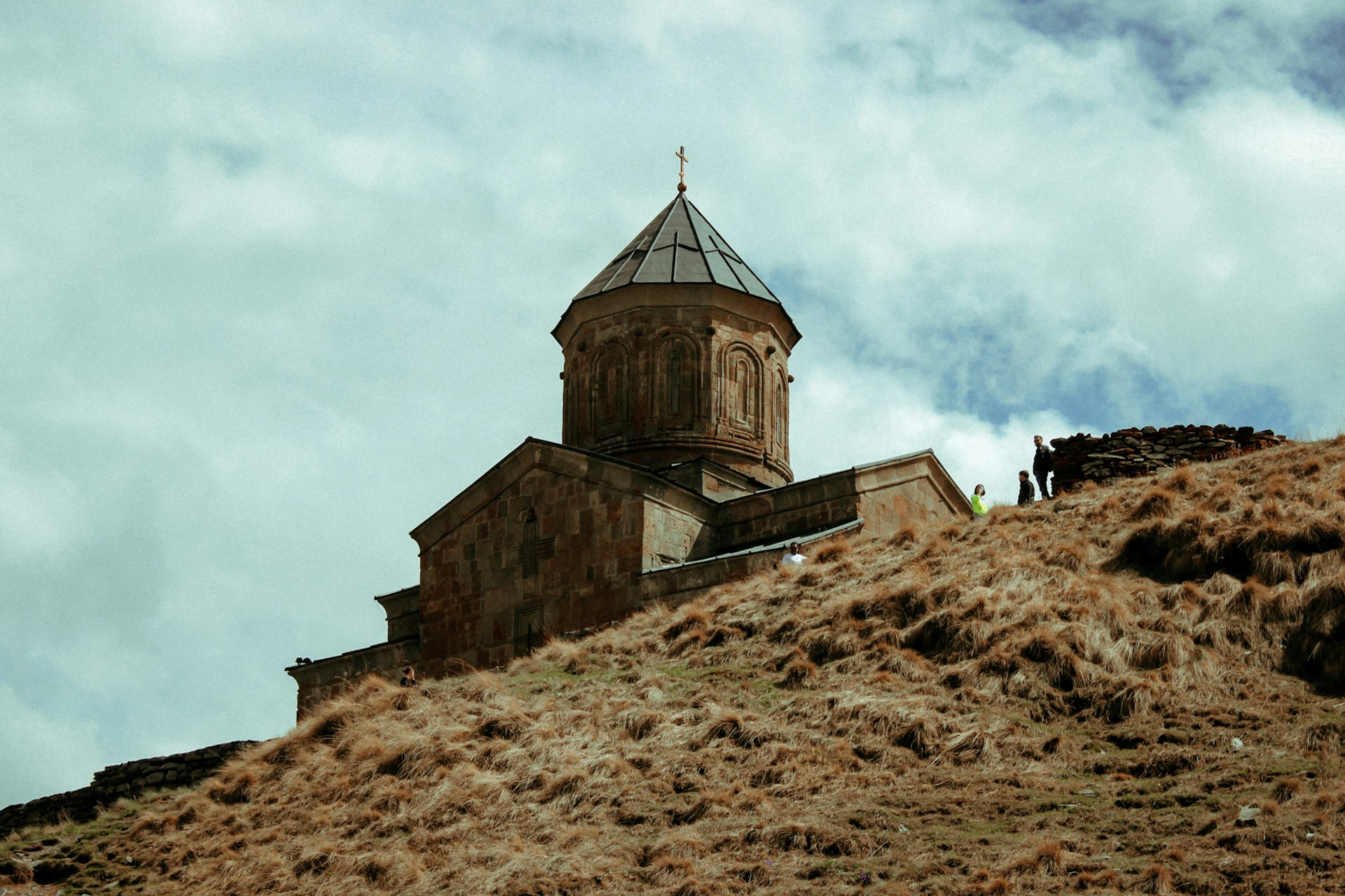 An ancient Georgian stone church with a domed bell tower and cross atop a hill